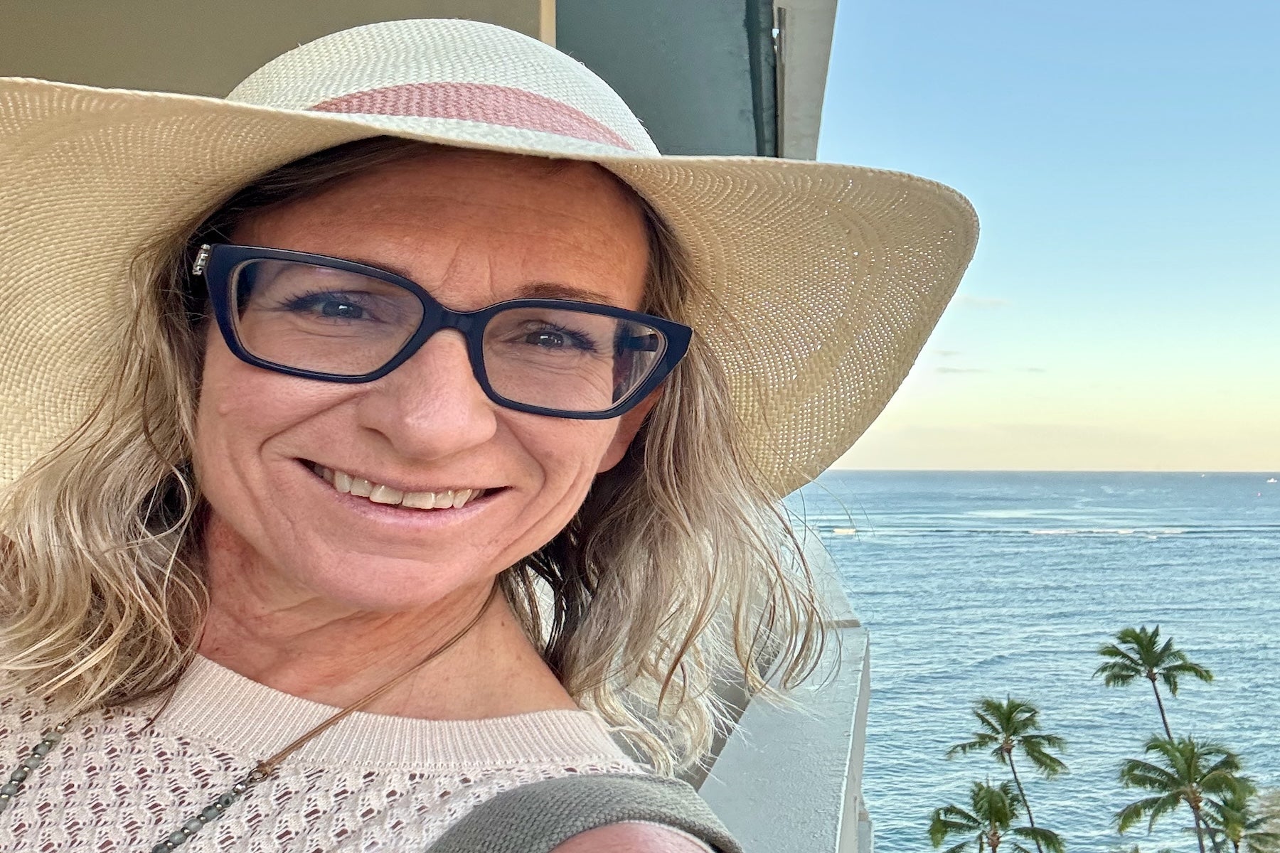 woman in a pretty straw hat smiling with ocean and palm trees in the background