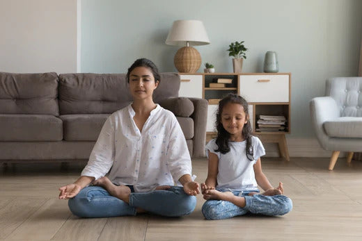 woman and child sitting cross legged on the floor with eyes closed meditating